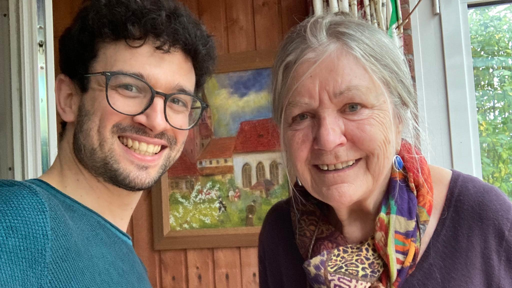 Ein Mann mit dunklen Locken und Brille und eine ältere Frau lächeln in die Kamera